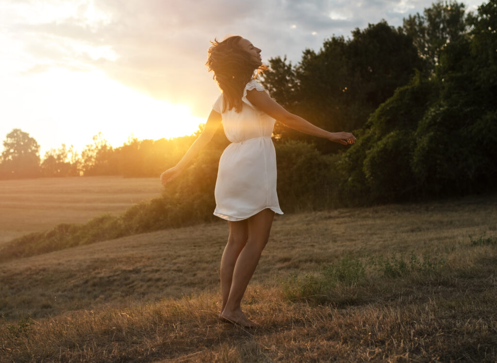 Natural photo of a woman walking calmly through nature with the sun behind her — evoking internal alignment and awareness.