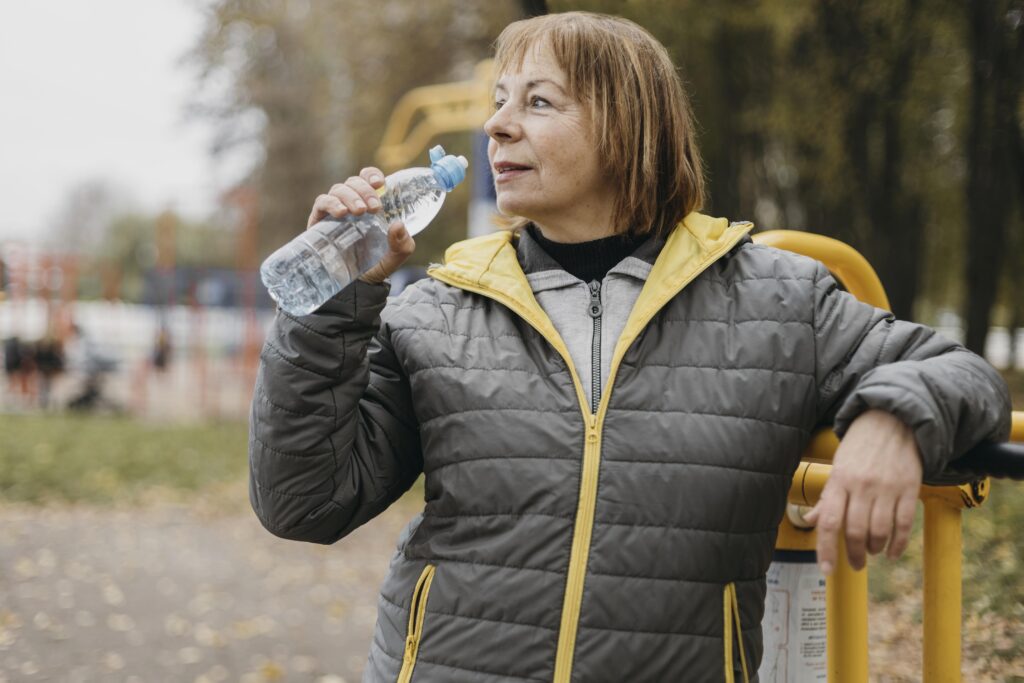 Natural photo of a woman in her 50s walking lightly down a tree-lined sidewalk, holding a water bottle.