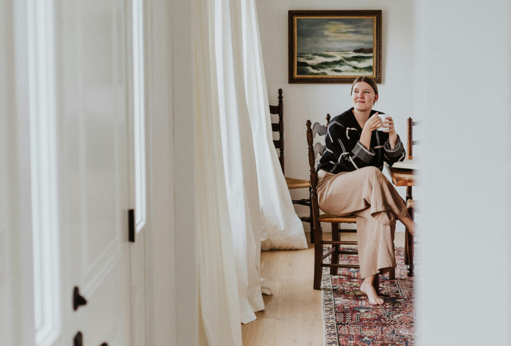 Woman at home, wrapped in a blanket, drinking tea with a thoughtful expression — evoking care and introspection.