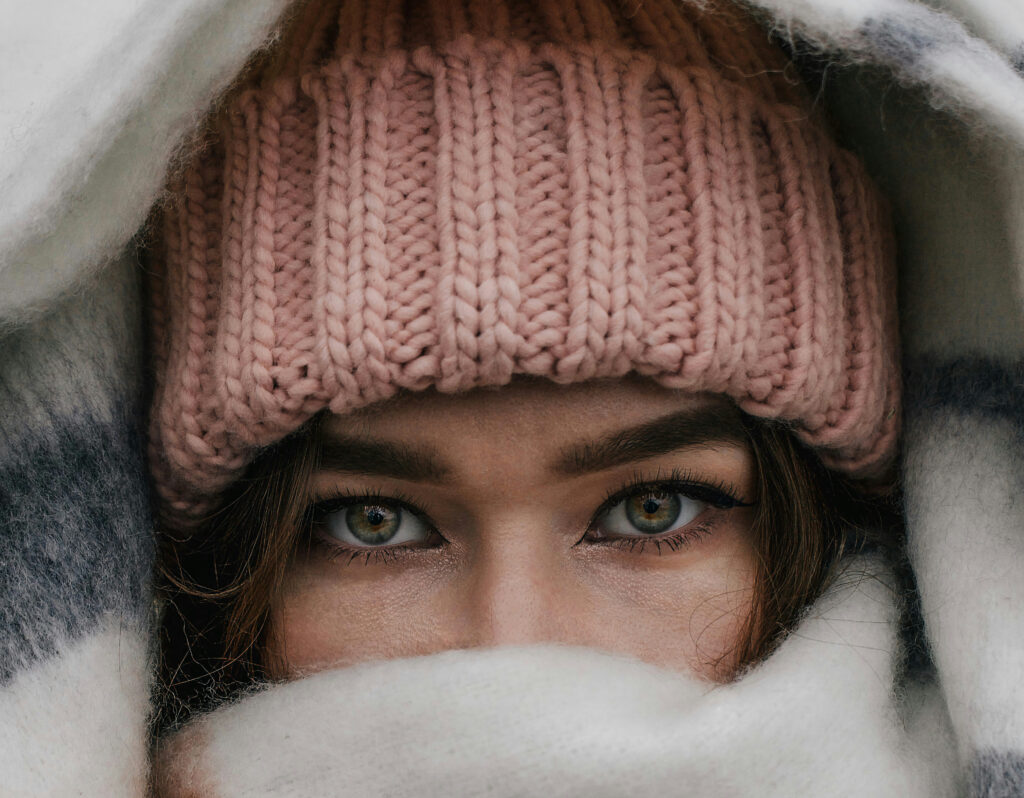Close-up of a woman’s hands holding a steaming cup of tea, wool socks visible — evoking winter warmth, self-care, and mindful rituals.
