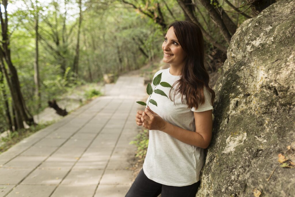 Natural photo of a woman outdoors, smiling while walking in nature, wearing casual clothes — symbolizing energy, calm, and well-being.
